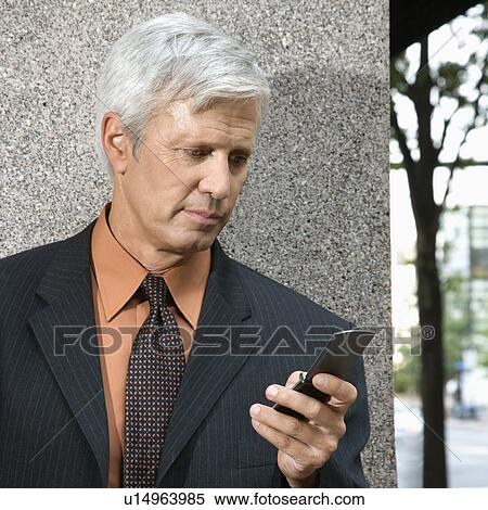 Stock Photography - Caucasian middle aged businessman looking down at cell phone.. Fotosearch