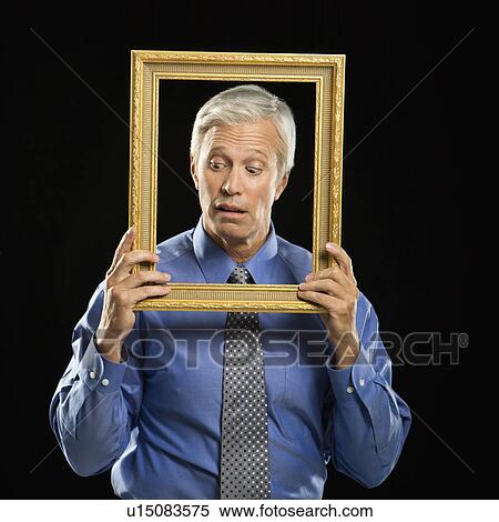 Stock Photography - Caucasian middle aged businessman holding empty picture frame in front of face making expression.. Fotosearch