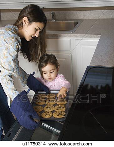 Caucasian mother and daughter taking cookies out of oven. View Large Photo Image Picture - Caucasian mother and daughter taking cookies out of oven.. Fotosearch