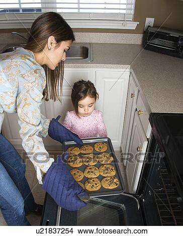 Caucasian mother and daughter taking cookies out of oven. View Large Photo Image Picture - Caucasian mother and daughter taking cookies out of oven.. Fotosearch