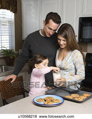 Stock Photo - Caucasian mother and father with daughter eating cookies and milk.. Fotosearch