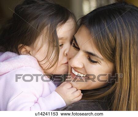 Stock Image - Caucasian mother holding daughter kissing her cheek and smiling.. Fotosearch