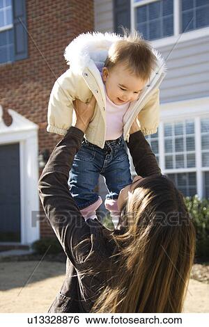 Caucasian mother holding up baby girl in front of house outside. View Large Photo Image Stock Photograph - Caucasian mother holding up baby girl in front of house outside.. Fotosearch