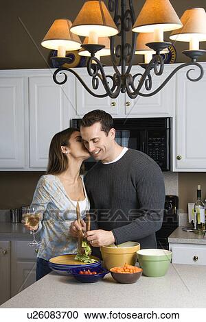 Stock Image - Caucasian woman kissing man at kitchen counter.. Fotosearch