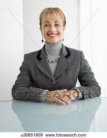 Stock Photo - Caucasian woman sitting at table smiling at viewer.. Fotosearch