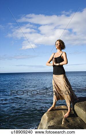 Stock Image - Caucasian young adult female meditating by the Pacific ocean of Maui, Hawaii.. Fotosearch