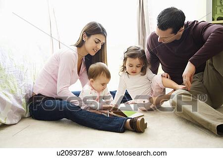 Stock Photo - Children with parents sitting on bedroom floor looking at book. Fotosearch