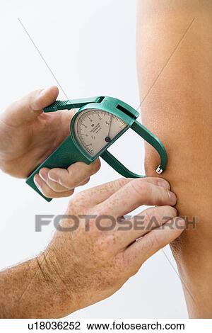 Stock Image - Close-up of adult male hand using caliper to test body fat.. Fotosearch