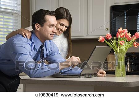 Stock Photo - Couple in kitchen looking at laptop computer. Fotosearch