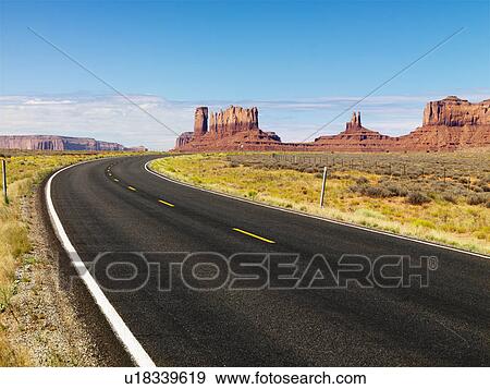 Curving scenic desert road with mesa land formations and mountains in the background View Large Photo Image Stock Photo - Curving scenic desert road with mesa land formations and mountains in the background. Fotosearch