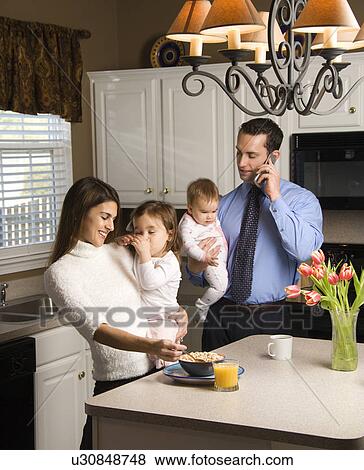 Stock Photo - Family in kitchen busy with children and cellphone. Fotosearch