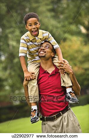 Stock Photo - Father carrying his son on his shoulders smiling and looking at eachother.. Fotosearch