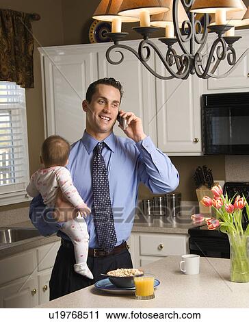 Father in holding baby and talking on cellphone in kitchen View Large Photo Image Stock Image - Father in holding baby and talking on cellphone in kitchen. Fotosearch