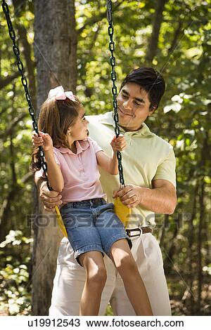 Stock Image - Father pushing daughter on swing and making eye contact. Fotosearch