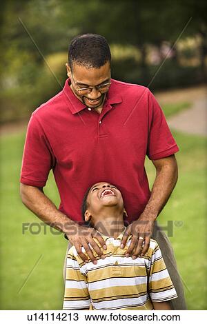 Stock Image - Father standing behind son with hands on his shoulders as boy smiles. Fotosearch