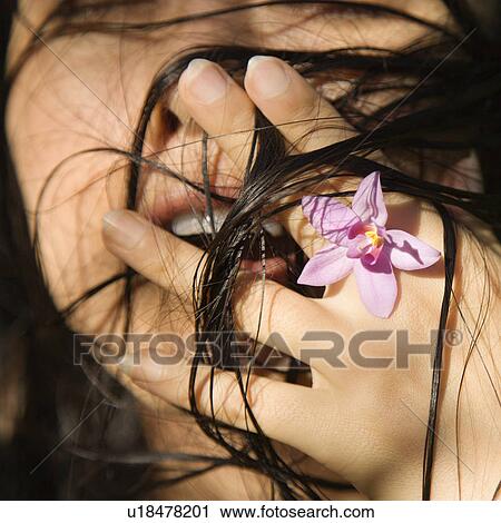 Stock Image - Female holding flower up to her face. Fotosearch