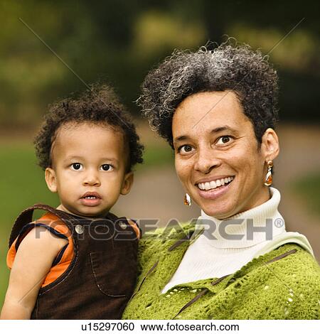 Stock Image - Head and shoulder portrait of woman holding boy and smiling. Fotosearch