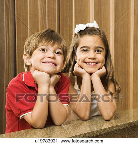 Stock Image - Hispanic children with their head on hands smiling at viewer. . Fotosearch