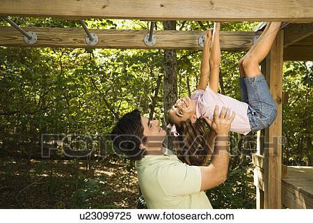 Hispanic girl hanging by arms and legs from monkey bars smiling at father helping her. View Large Photo Image Stock Photography - Hispanic girl hanging by arms and legs from monkey bars smiling at father helping her.. Fotosearch