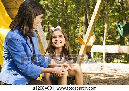 Hispanic girl sitting on playground slide smiling at woman applying first aid bandage to knee. View Large Photo Image Stock Image - Hispanic girl sitting on playground slide smiling at woman applying first aid bandage to knee.. Fotosearch
