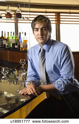 Stock Photo - Hispanic mid adult man leaning on bar with martini looking at viewer.. Fotosearch