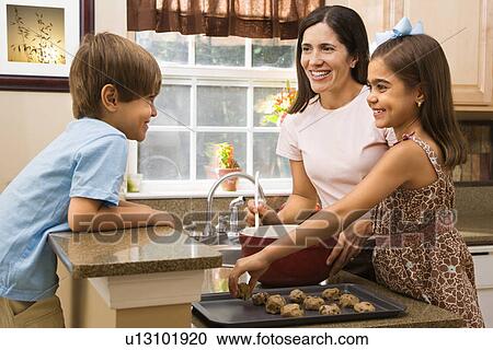 Stock Image - Hispanic mother and children in kitchen making cookies.. Fotosearch