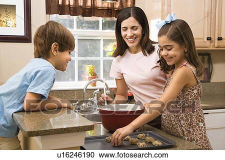Stock Image - Hispanic mother and children in kitchen making cookies.. Fotosearch