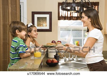Hispanic mother handing healthy breakfast to young children in home kitchen. View Large Photo Image Picture - Hispanic mother handing healthy breakfast to young children in home kitchen.. Fotosearch