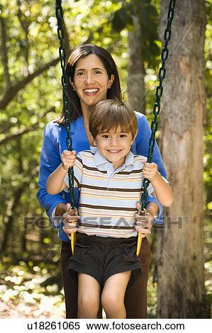 Hispanic mother pushing son on swing and smiling at viewer. View Large Photo Image Stock Photography - Hispanic mother pushing son on swing and smiling at viewer.. Fotosearch