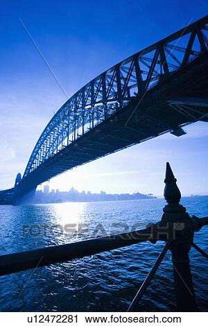 Stock Image - Low angle view of Sydney Harbour Bridge at dusk with harbour and distant Sydney skyline, Australia. Fotosearch
