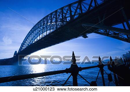 Stock Image - Low angle view of Sydney Harbour Bridge at dusk with harbour and distant Sydney skyline, Australia. Fotosearch