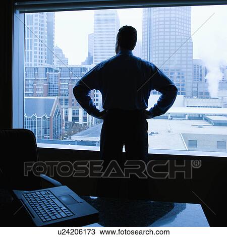 Stock Image - Male with hands on his hips in office with skyline in background. Fotosearch