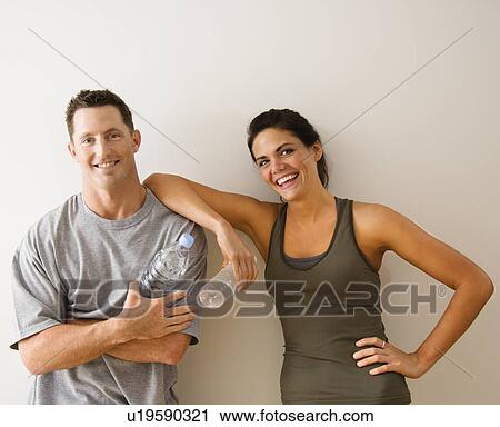 Stock Image - Man and woman at gym in fitness attire holding water bottles. Fotosearch