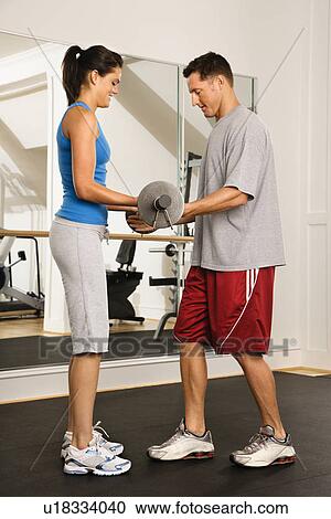 Stock Image - Man and woman lifting weights in gym. Fotosearch