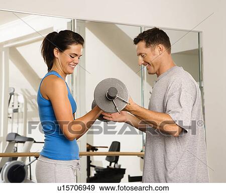 Stock Photo - Man and woman lifting weights in gym. Fotosearch