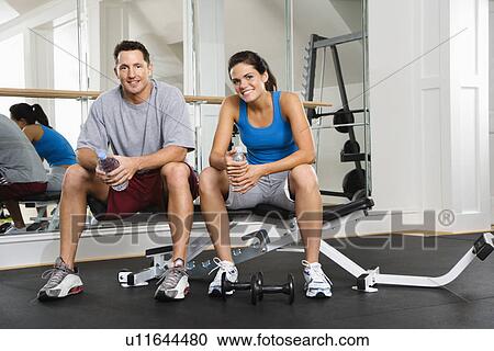 Stock Image - Man and woman sitting on exercise machine . Fotosearch