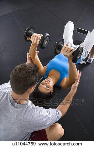 Stock Photo - Man assisting woman lifting weights at gym.. Fotosearch