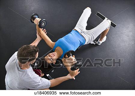 Stock Photography - Man assisting woman lifting weights at gym.. Fotosearch