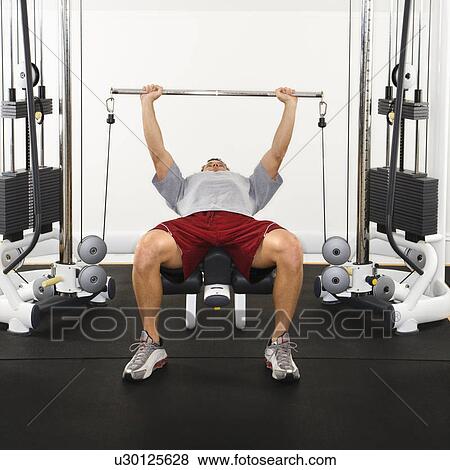 Stock Photo - Man at gym lifting weights on weight machine.. Fotosearch
