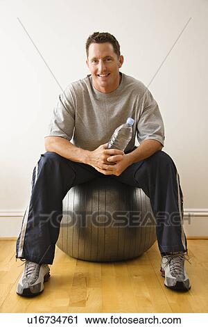 Man holding bottle sitting on balance ball at gym View Large Photo Image Stock Image - Man holding bottle sitting on balance ball at gym. Fotosearch