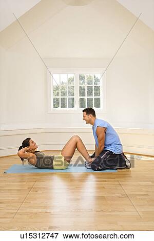 Stock Photo - Man holding woman's feet down as she does sit up exercises. Fotosearch