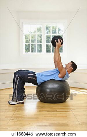 Stock Photography - Man lifting medicine ball while on balance ball.. Fotosearch