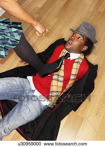 Stock Image - Man on back on floor with woman stepping on him and pointing accusingly. Fotosearch