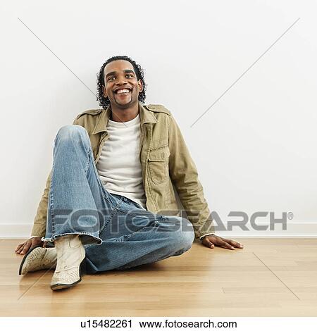 Stock Image - Man sitting on wood floor of home smiling. Fotosearch