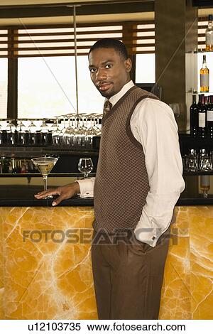 Stock Photography - Man standing at bar with martini looking at viewer. Fotosearch