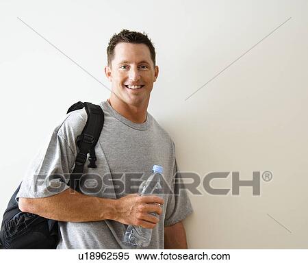 Stock Photography - Man standing smiling with gym bag and bottled water.. Fotosearch