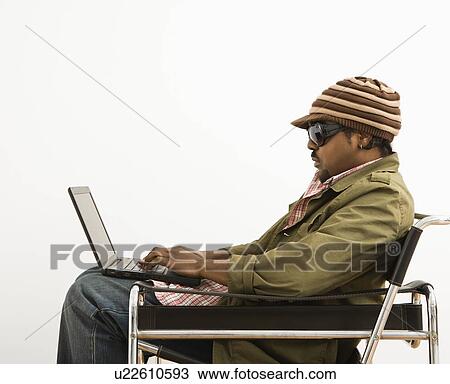 Stock Image - Man wearing hat and typing on laptop computer. Fotosearch