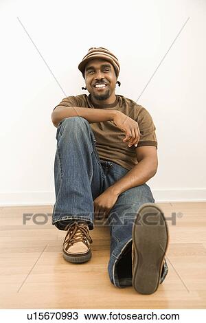 Stock Image - Man wearing hat sitting on floor. Fotosearch