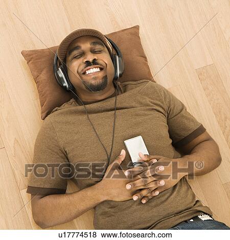 Man wearing headphones and listening to mp3 player while lying on back on floor View Large Photo Image Stock Photo - Man wearing headphones and listening to mp3 player while lying on back on floor. Fotosearch