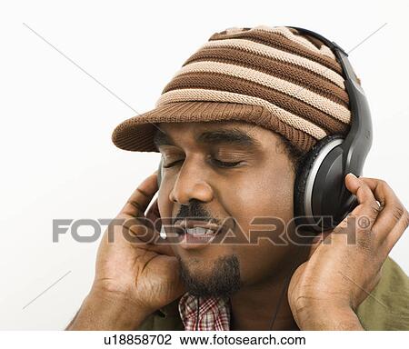 Stock Image - Man wearing knit hat and listening to headphones with eyes closed. Fotosearch